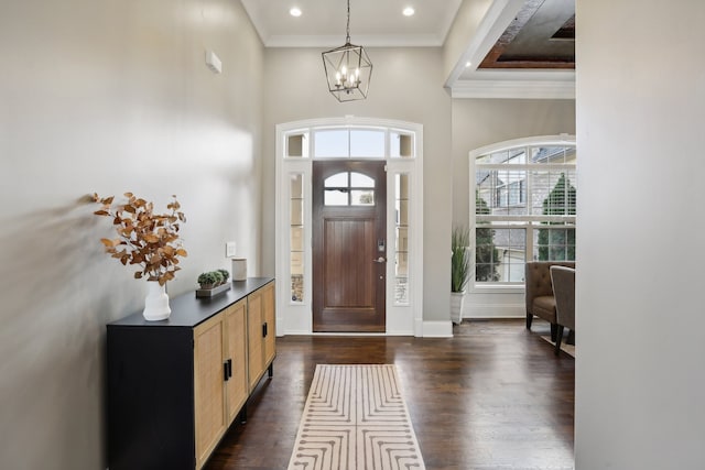 foyer with a high ceiling, a raised ceiling, dark hardwood / wood-style floors, a chandelier, and ornamental molding