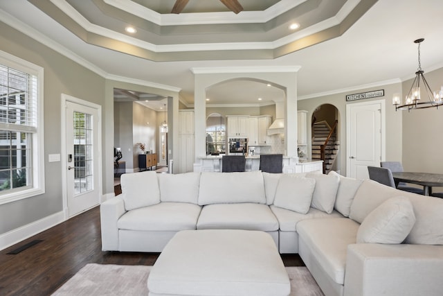 living room with a tray ceiling, crown molding, dark hardwood / wood-style flooring, and an inviting chandelier