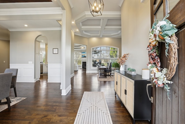 foyer with dark wood-type flooring, an inviting chandelier, coffered ceiling, crown molding, and beam ceiling