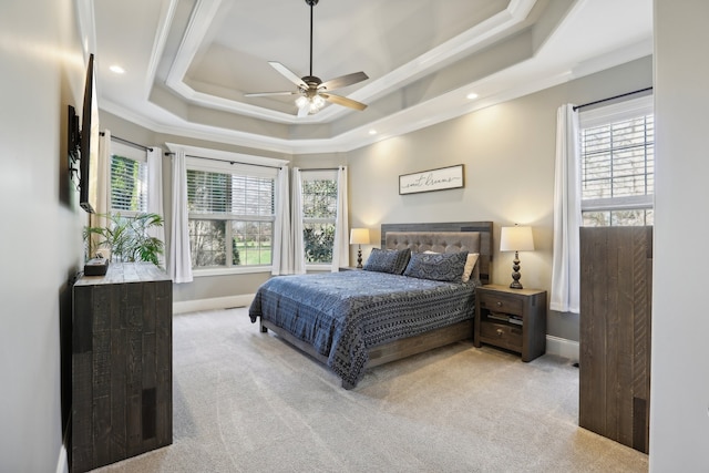 bedroom featuring light carpet, a tray ceiling, multiple windows, and ceiling fan