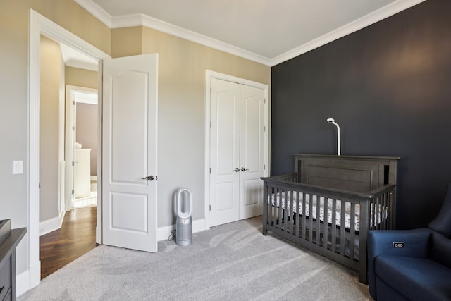 bedroom featuring a crib, crown molding, light carpet, and a closet