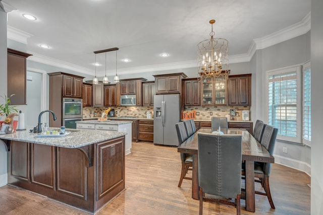 kitchen with appliances with stainless steel finishes, light wood-type flooring, light stone counters, and pendant lighting