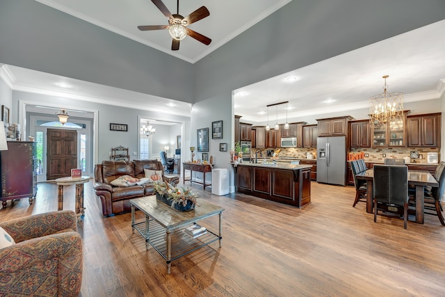 living room with light hardwood / wood-style flooring, a towering ceiling, ceiling fan with notable chandelier, and ornamental molding