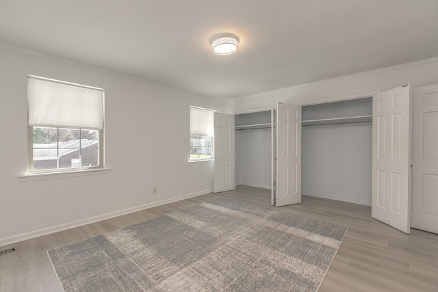 unfurnished bedroom featuring light wood-type flooring, ornamental molding, and multiple windows