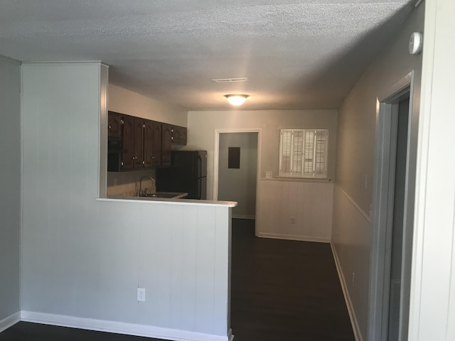 kitchen with dark brown cabinetry, black fridge, dark hardwood / wood-style flooring, kitchen peninsula, and a textured ceiling