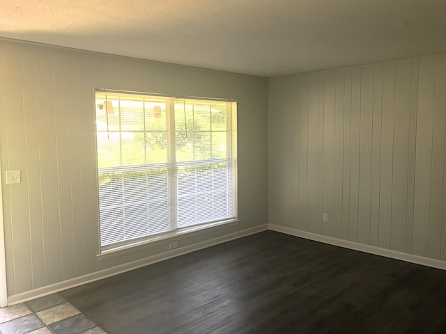 unfurnished room with dark hardwood / wood-style flooring, a textured ceiling, and wooden walls