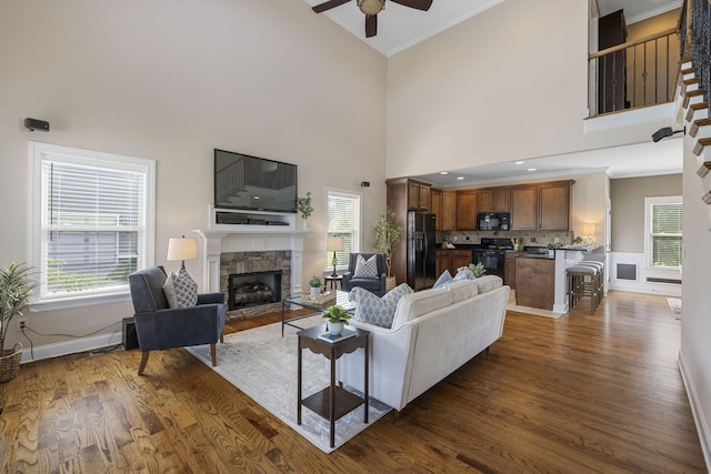 living room featuring dark hardwood / wood-style floors, a towering ceiling, a fireplace, and ornamental molding