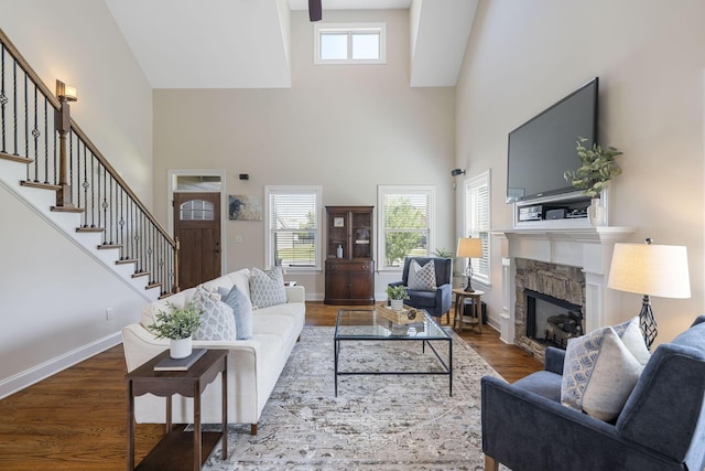 living room with dark hardwood / wood-style floors, a stone fireplace, and a high ceiling