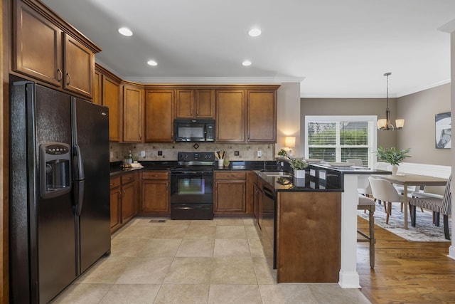 kitchen with kitchen peninsula, crown molding, decorative light fixtures, decorative backsplash, and black appliances