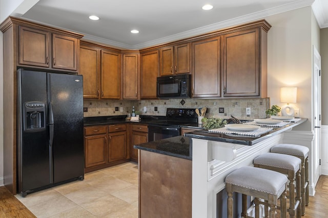 kitchen with backsplash, dark stone countertops, crown molding, a breakfast bar, and black appliances