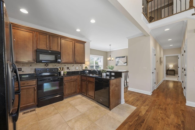 kitchen featuring black appliances, ornamental molding, decorative light fixtures, light hardwood / wood-style floors, and kitchen peninsula