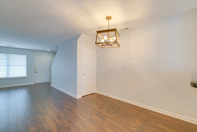 spare room with a notable chandelier, dark hardwood / wood-style floors, and a textured ceiling