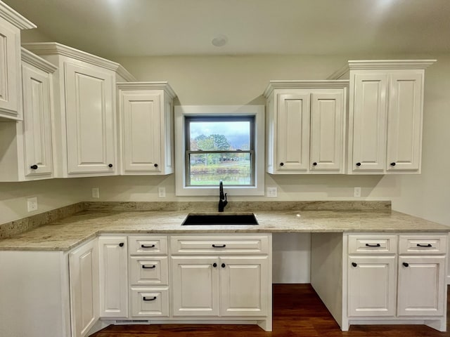 kitchen featuring light stone countertops, white cabinetry, and sink