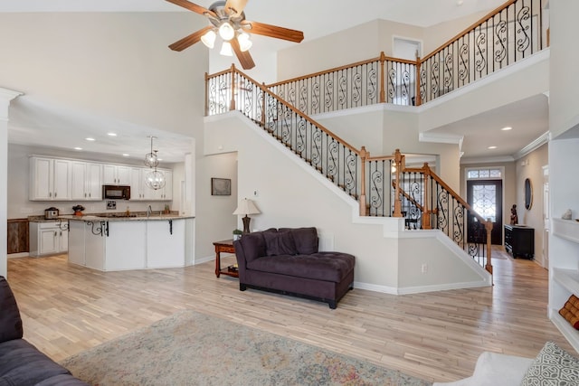 living room with ceiling fan, light hardwood / wood-style floors, ornamental molding, and a high ceiling