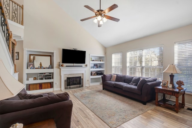 living room with built in features, light hardwood / wood-style floors, high vaulted ceiling, and ceiling fan