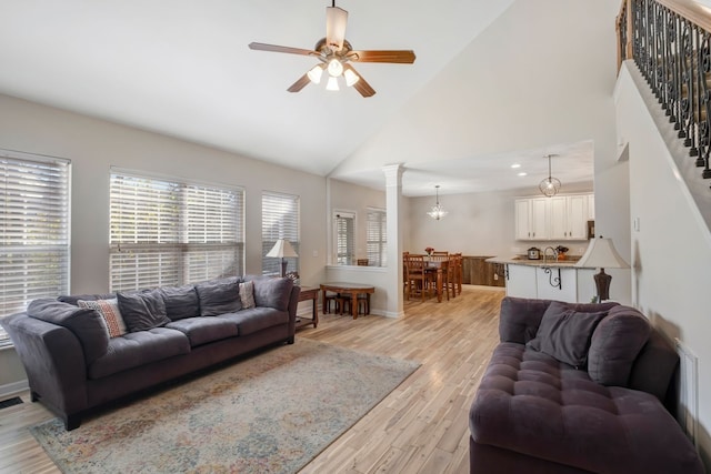 living room featuring ceiling fan, sink, high vaulted ceiling, decorative columns, and light wood-type flooring