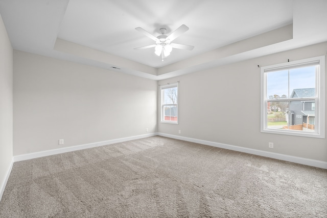 empty room with carpet flooring, a tray ceiling, ceiling fan, and a healthy amount of sunlight