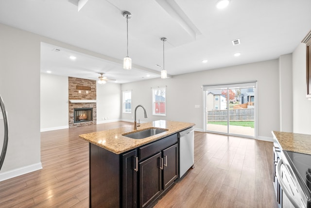 kitchen featuring stainless steel dishwasher, plenty of natural light, a kitchen island with sink, sink, and hanging light fixtures