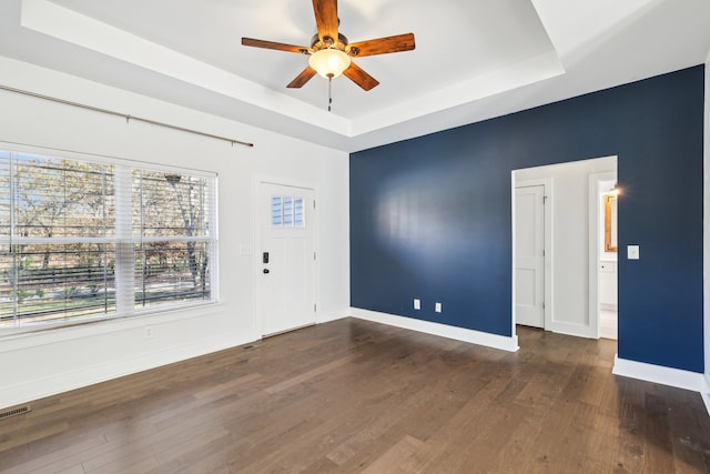 empty room with a tray ceiling, ceiling fan, and dark hardwood / wood-style flooring