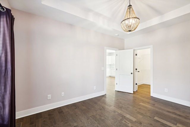 spare room with a raised ceiling, an inviting chandelier, and dark wood-type flooring