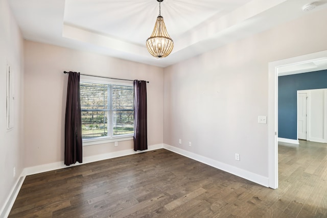 spare room with a raised ceiling, dark hardwood / wood-style flooring, and a notable chandelier