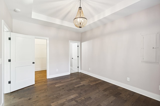 spare room with a raised ceiling, dark wood-type flooring, electric panel, and an inviting chandelier