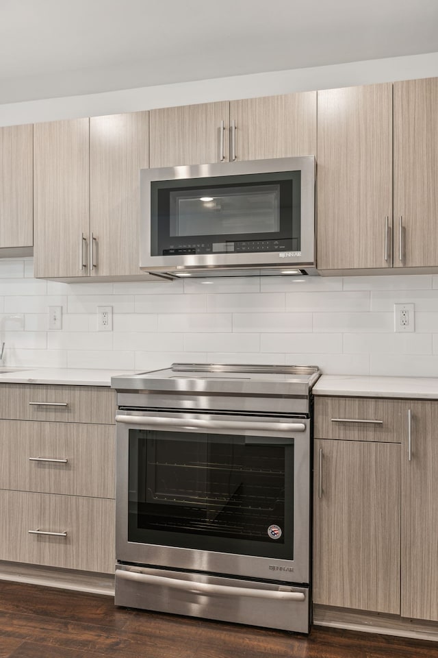 kitchen with light brown cabinets, backsplash, stainless steel appliances, and dark hardwood / wood-style floors