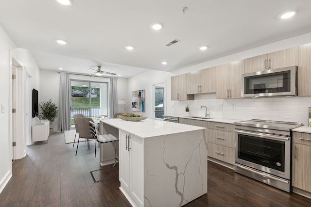 kitchen with appliances with stainless steel finishes, ceiling fan, sink, a center island, and dark hardwood / wood-style floors