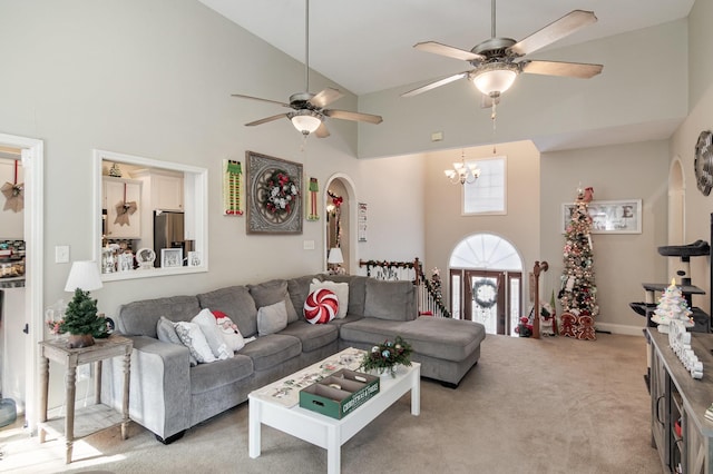 carpeted living room featuring ceiling fan with notable chandelier and high vaulted ceiling