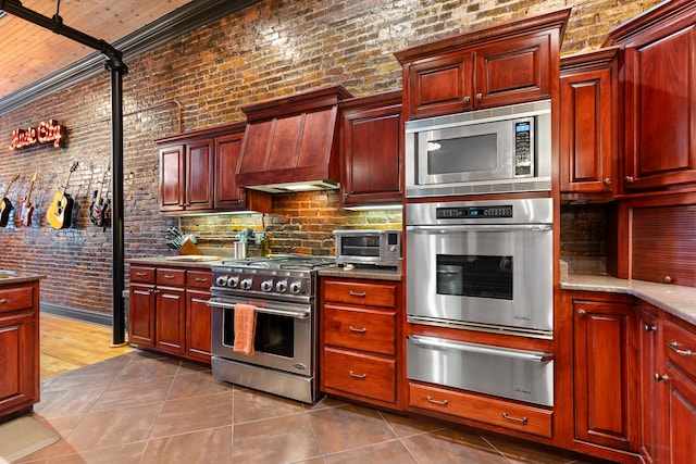 kitchen featuring appliances with stainless steel finishes, premium range hood, brick wall, dark tile patterned floors, and crown molding