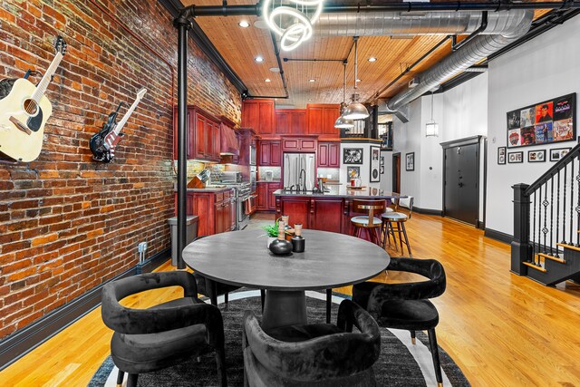 dining room with a high ceiling, sink, light hardwood / wood-style floors, and brick wall