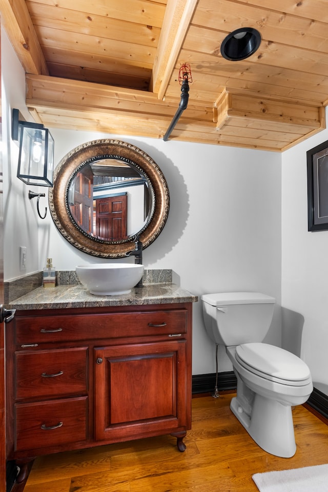 bathroom with beam ceiling, wood-type flooring, toilet, vanity, and wood ceiling