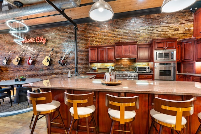 kitchen featuring brick wall, light wood-type flooring, sink, and appliances with stainless steel finishes