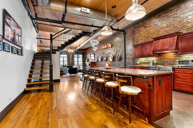 bar featuring custom exhaust hood, a high ceiling, hanging light fixtures, light wood-type flooring, and brick wall