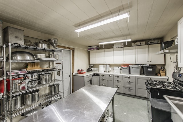 kitchen with black gas stove, gray cabinets, wall chimney exhaust hood, and stainless steel counters