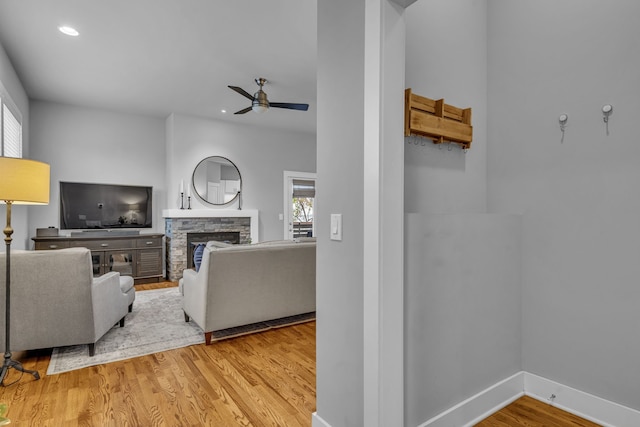 living room featuring a stone fireplace, ceiling fan, and hardwood / wood-style floors