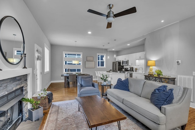 living room with a stone fireplace, ceiling fan, light hardwood / wood-style flooring, and sink