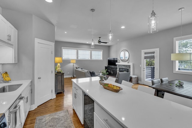 kitchen with a stone fireplace, ceiling fan, white cabinets, and light hardwood / wood-style floors