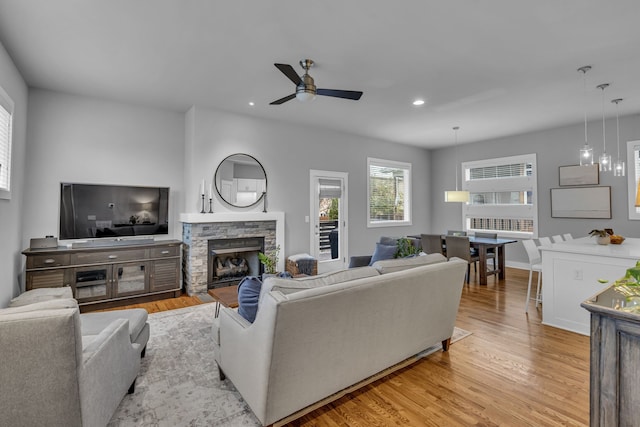 living room with ceiling fan, a stone fireplace, and light hardwood / wood-style flooring