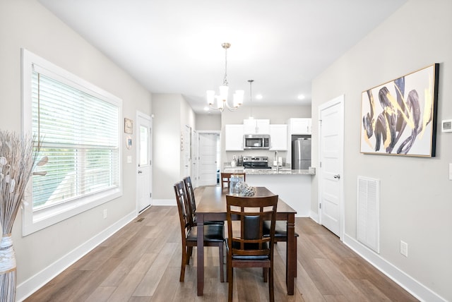 dining space with sink, a notable chandelier, and light wood-type flooring