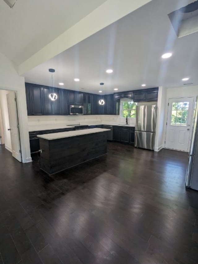 kitchen with a center island, sink, appliances with stainless steel finishes, decorative light fixtures, and dark hardwood / wood-style flooring