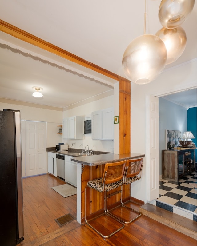 kitchen with white cabinets, kitchen peninsula, ornamental molding, appliances with stainless steel finishes, and wood-type flooring