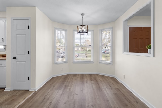 unfurnished dining area with a notable chandelier and light wood-type flooring