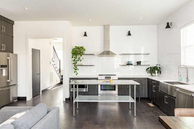 kitchen with dark wood-type flooring, sink, wall chimney exhaust hood, appliances with stainless steel finishes, and dark brown cabinets