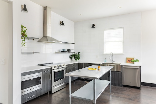 kitchen featuring light countertops, appliances with stainless steel finishes, modern cabinets, wall chimney exhaust hood, and a sink