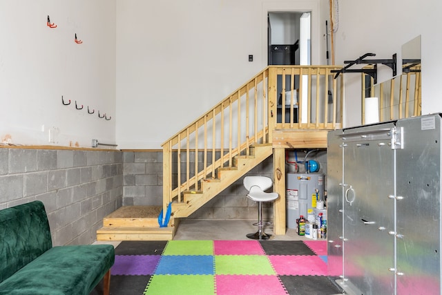 stairway featuring water heater, concrete block wall, concrete flooring, and a high ceiling