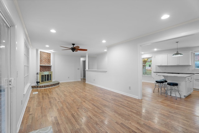 unfurnished living room with light hardwood / wood-style flooring, ornamental molding, and a brick fireplace