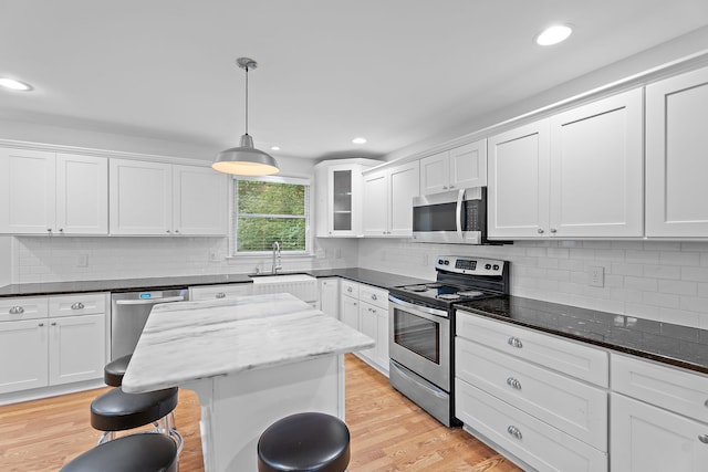 kitchen with appliances with stainless steel finishes, sink, dark stone countertops, white cabinets, and light hardwood / wood-style floors