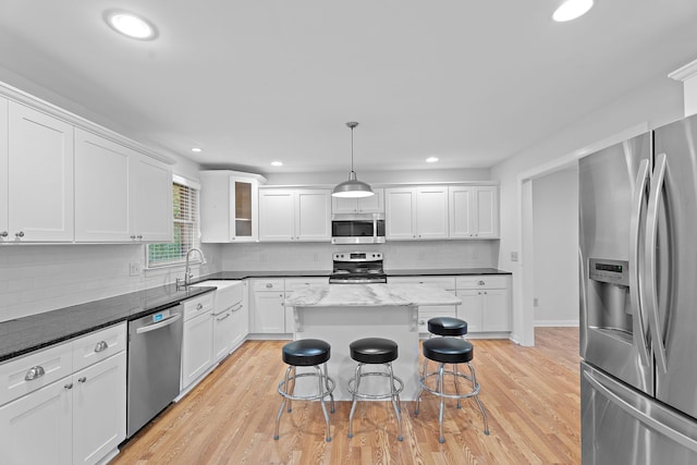 kitchen with appliances with stainless steel finishes, a breakfast bar, sink, pendant lighting, and light hardwood / wood-style floors