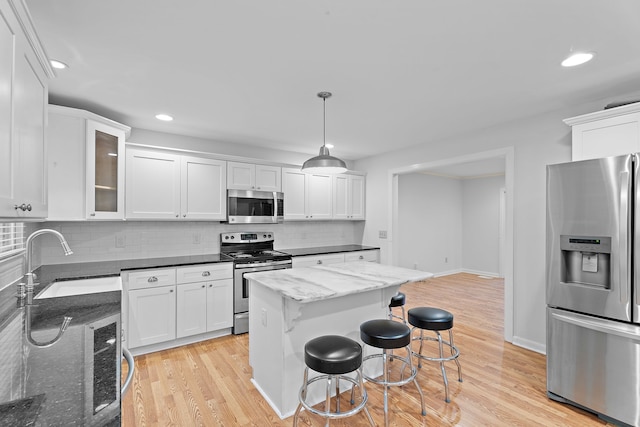 kitchen featuring dark stone countertops, light hardwood / wood-style flooring, stainless steel appliances, and decorative light fixtures